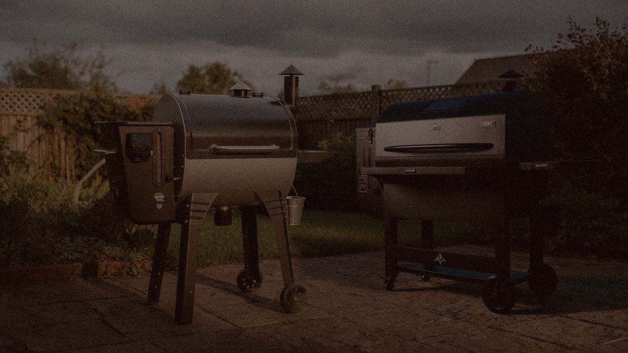 Camp Chef Woodwind Pro WiFi 24 and Green Mountain Grills Peak at night with smoke, wood pellet grills on a dark patio