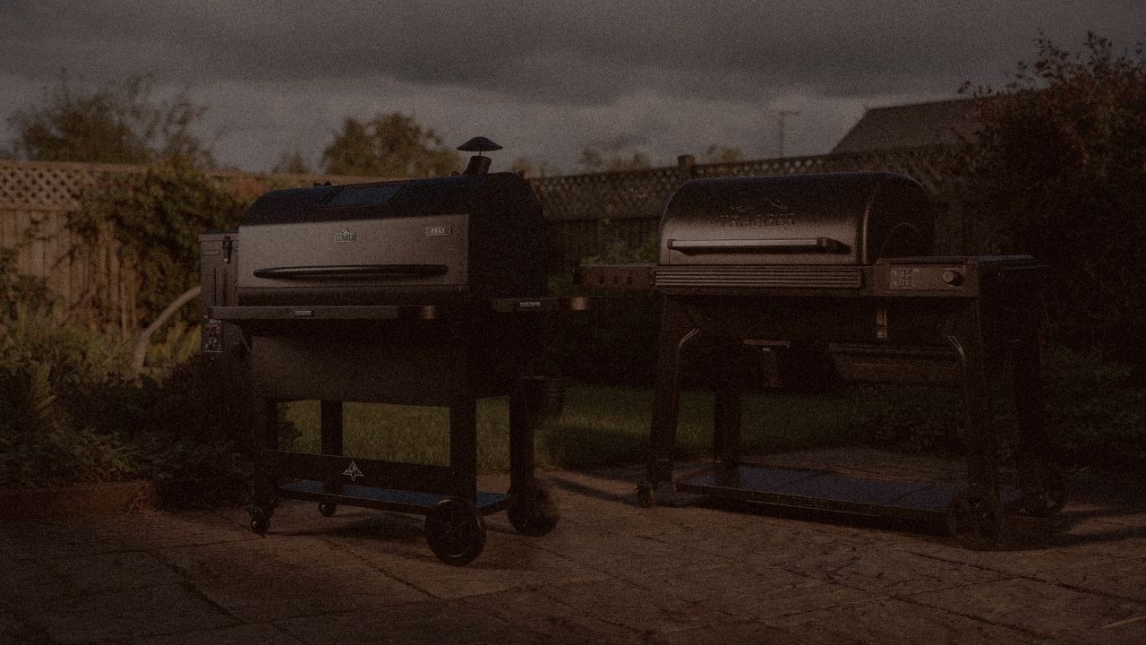 Green Mountain Grills Peak and Traeger Woodridge Pro at night with smoke, wood pellet grills on a dark patio