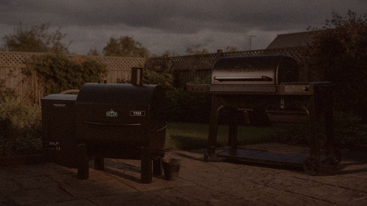 Green Mountain Grills Trek and Traeger Woodridge Pro at night with smoke, wood pellet grills on a dark patio