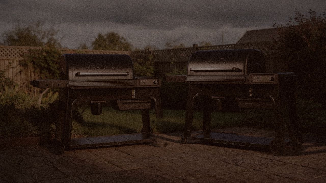 Traeger Ironwood and Traeger Woodridge Pro at night with smoke, wood pellet grills on a dark patio